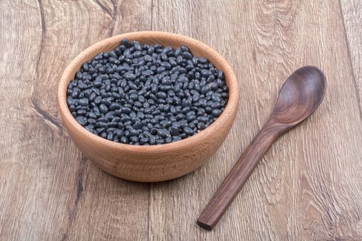 Bowl with beans and wooden spoon on a brown wooden background