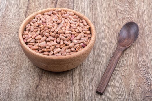 Bowl with beans and wooden spoon on a brown wooden background