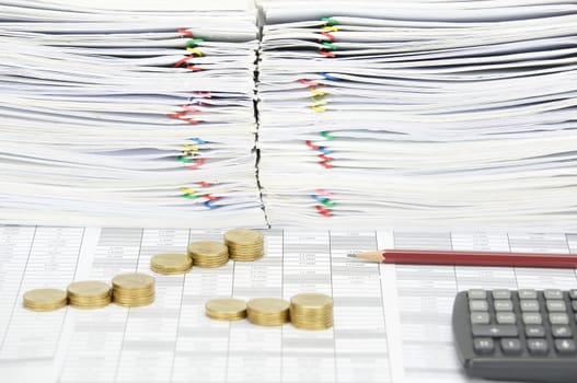 Brown pencil and step pile of gold coins on finance account have blur calculator with overload of paperwork as foreground and background.