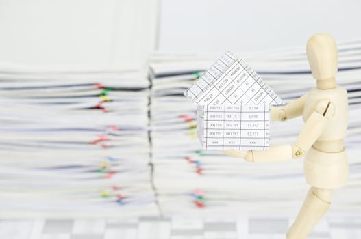 Wooden dummy holding house on finance account have blur overload of paperwork as background.