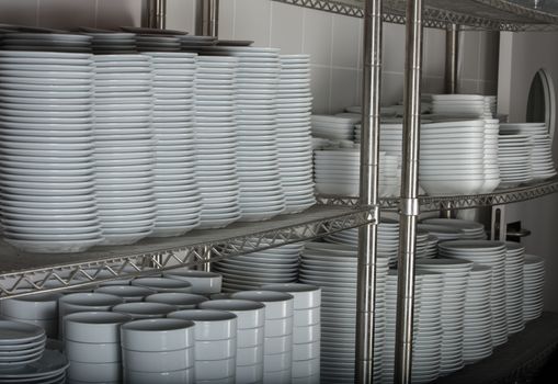 stacks of many white plates on a wire rack shelf in a commercial kitchen