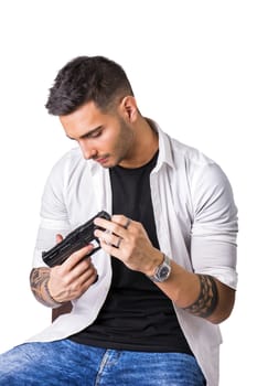 Young handsome man holding a hand gun, wearing black t-shirt, isolated on white background in studio