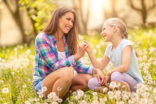 Happy cute little girl with mother holding dandelion in the park.