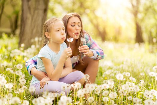 Happy cute little girl blowing dandelion with mother in the park.