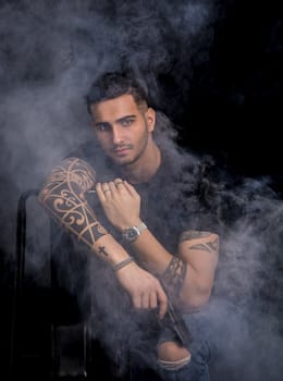 Young handsome man holding a hand gun, wearing black t-shirt, on dark background in studio