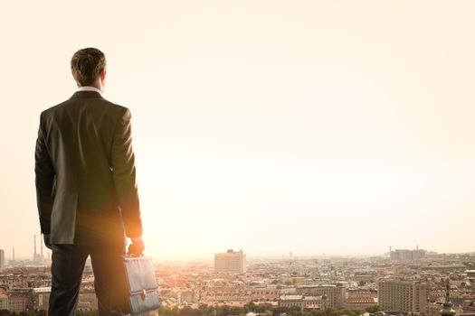 Businessman standing with back against morning city, panoramic view
