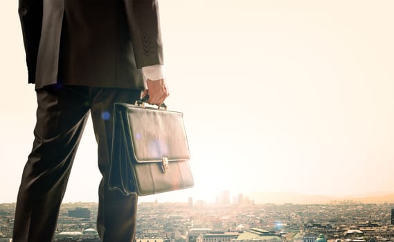 Businessman with suitcase standing with back against morning city, panoramic view
