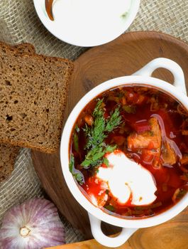 Traditional Soup Borscht with Beet, Vegetables and Meat. Top View of Borscht in Bowl closeup on Wooden Plate with Brown Bread, Garlic and Sour Cream