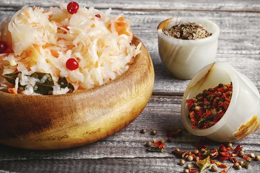 Wooden barrel with sauerkraut and scattered on a background of spices