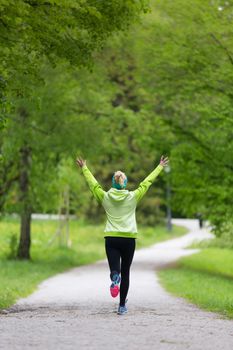 I have made it. Sporty young female runner arms rised in city park.  Running woman during outdoor workout in nature. Fitness model outdoors. Weight Loss. Healthy lifestyle. 