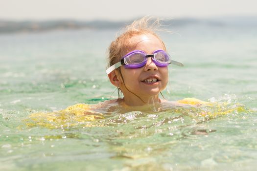 Cute little girl swimming with armbands and goggles in the sea