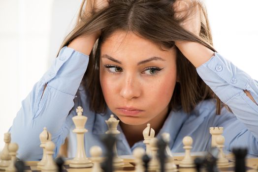 Young beautiful businesswoman devises Business strategy. She sitting above the chessboard with figures and thinking.