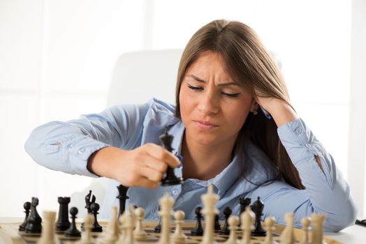 Young beautiful businesswoman devises Business strategy. She sitting above the chessboard with figures and thinking.