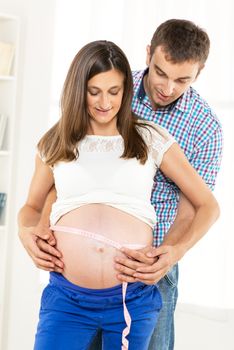 Happy couple measuring on pregnant woman's belly