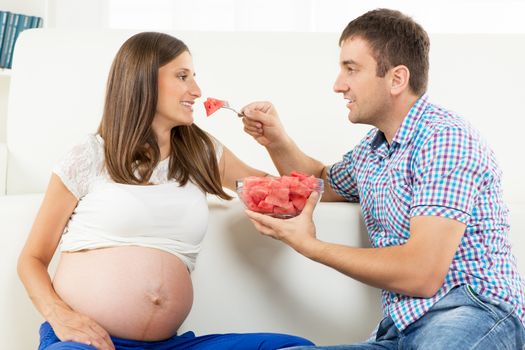 Happy Pregnant woman and her husband eating watermelon