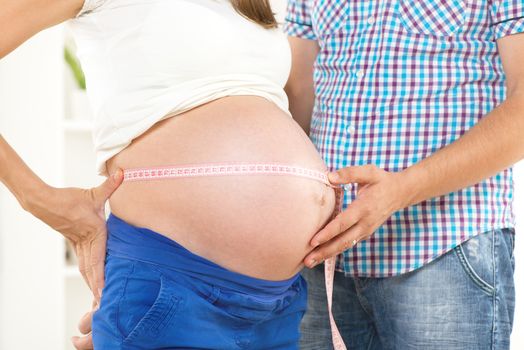 Male and female hands measuring on pregnant woman's belly .