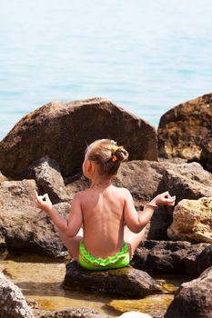 Little girl doing yoga on rocks by the sea