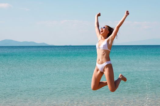 Happy young beautiful woman jumping on the beach with hands up 