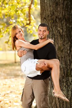 Young man holding a beautiful girl on his arms in nature