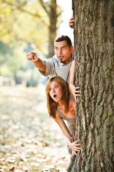 Young couple behind tree looking something scary