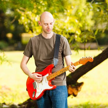 Young guitarist, playing guitar in beautiful nature environment