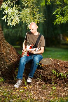 Young guitarist, playing guitar in beautiful nature environment