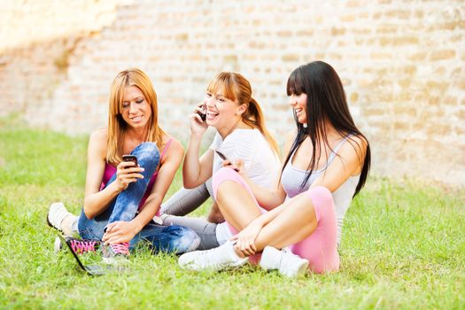 Three young beautiful girls communicate with cell phone outdoor