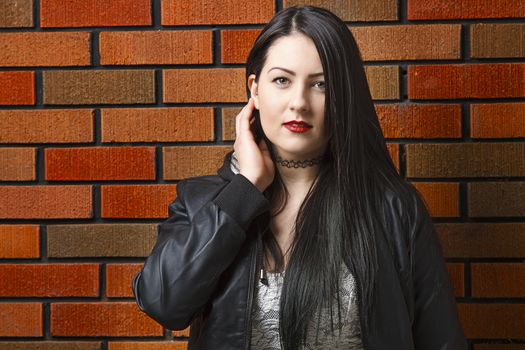 young twenty year old woman adjusting her hair against a brick wall