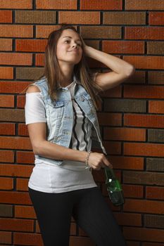 early twenties woman against a bick wall, holding green bottle of beer