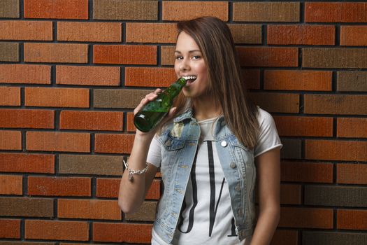 twenty something girl leaning against wall drinking a beer