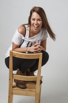 young brunette woman crouching on a chair, laughing