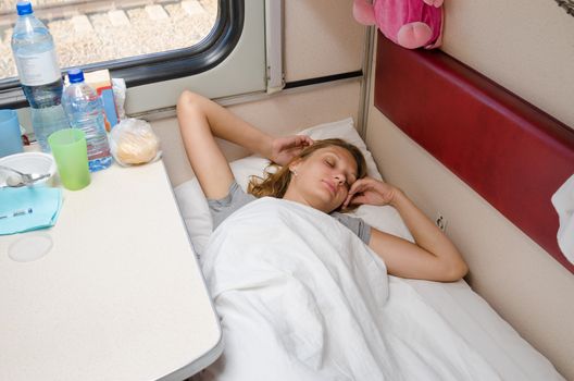 Girl sleeps in train arms outstretched on the lower second-class place car coupe