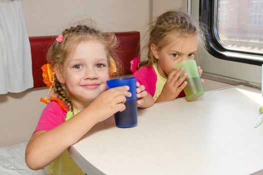 Two little sisters in a train drinking tea at a table on the lower place in the second-class compartment wagon