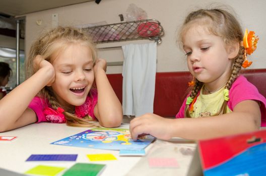 Two girls having fun playing on the train at the table on the lower place in the second-class compartment wagon