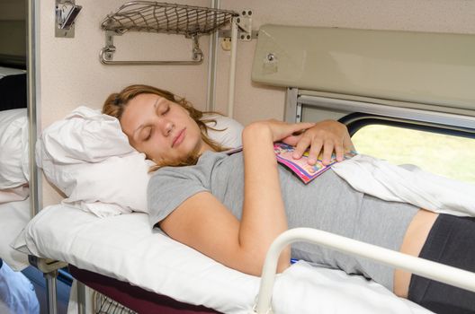 The girl in a train sleeping at the back on the top shelf and the side with the magazine in an embrace