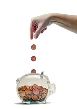 Great idea or concept for feeding the piggy bank or just saving money. Many pennies filling up a clear piggy bank. Hand shown dropping pennies in. Isolated on white. Studio shot