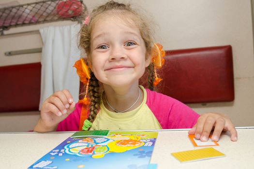 Little girl on the train with a happy smile sitting at a table on the lower second-class place car and makes the applique