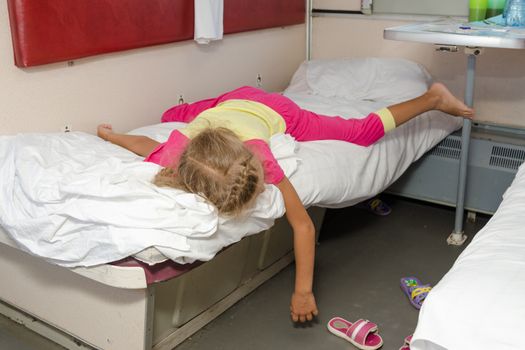 Little girl on the train lies flat on the lower second-class place car dangling arm and a leg