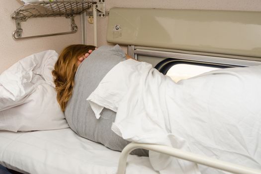 The girl sleeps on the top shelf of the side seats in the second-class carriage turned to the wall