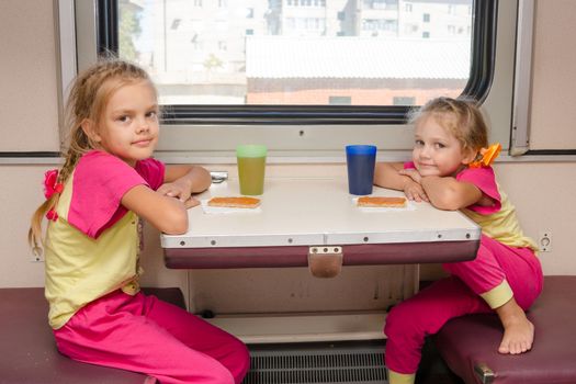 Two little girls on the train sitting at the table in the outboard second-class car in the same clothes