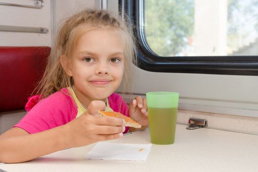 Six-year girl drinking tea with a sandwich on the train at the table on outboard second-class carriage