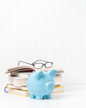 Pile of textbooks and a blue porcelain piggybank.  Suggests the concept of the cost of education.