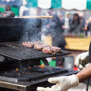 Chef making beef burgers outdoor on open kitchen international food festival event. Street food ready to serve on a food stall.