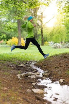 Sporty young female runner jumping the stream in city park.  Running woman. Female runner during outdoor workout in nature. Fitness model outdoors. Weight Loss. Healthy lifestyle. 