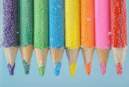 Colorful pencils close-up into water with bubbles