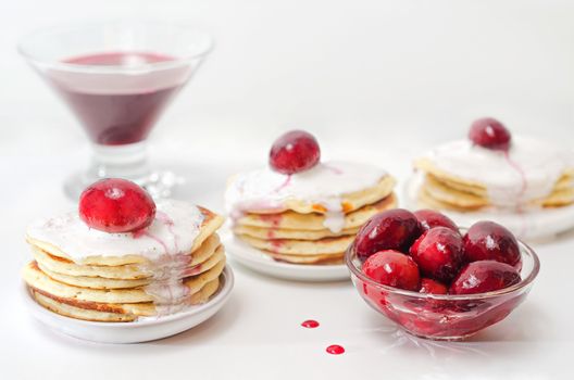 Three plates with small pancakes, decorated with plums out of the jam. Plum jam and syrup in the bowl. High key bokeh.