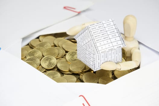 Wooden dummy holding house have surrounded by stack of gold coins and overload of paperwork as background.