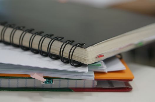 Black notebook and stack of report document placed on desk in office.