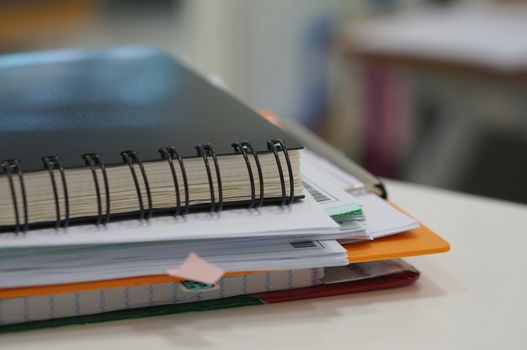 Stack of paperwork and black notebook placed on desk at office.