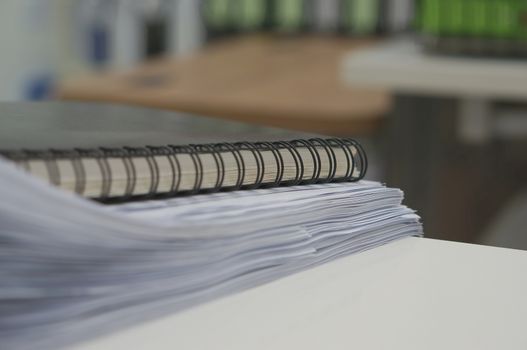 Black notebook and stack of white document on desk in office.